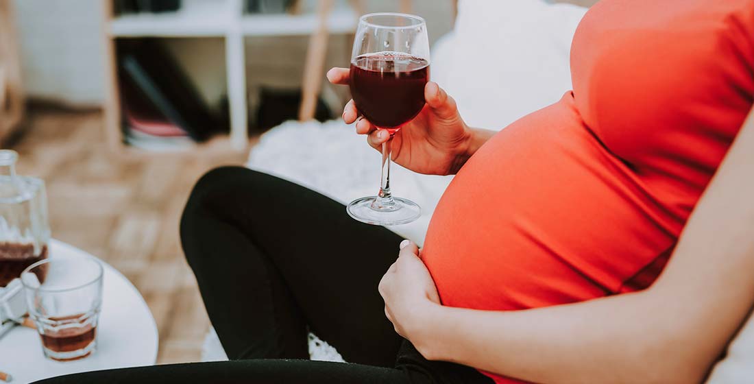 беременная женщина с бокалом вина в руке сидит на диване