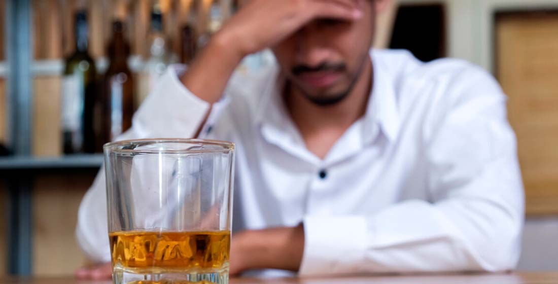 грустный мужчина сидит за столом перед стаканом с алкоголем